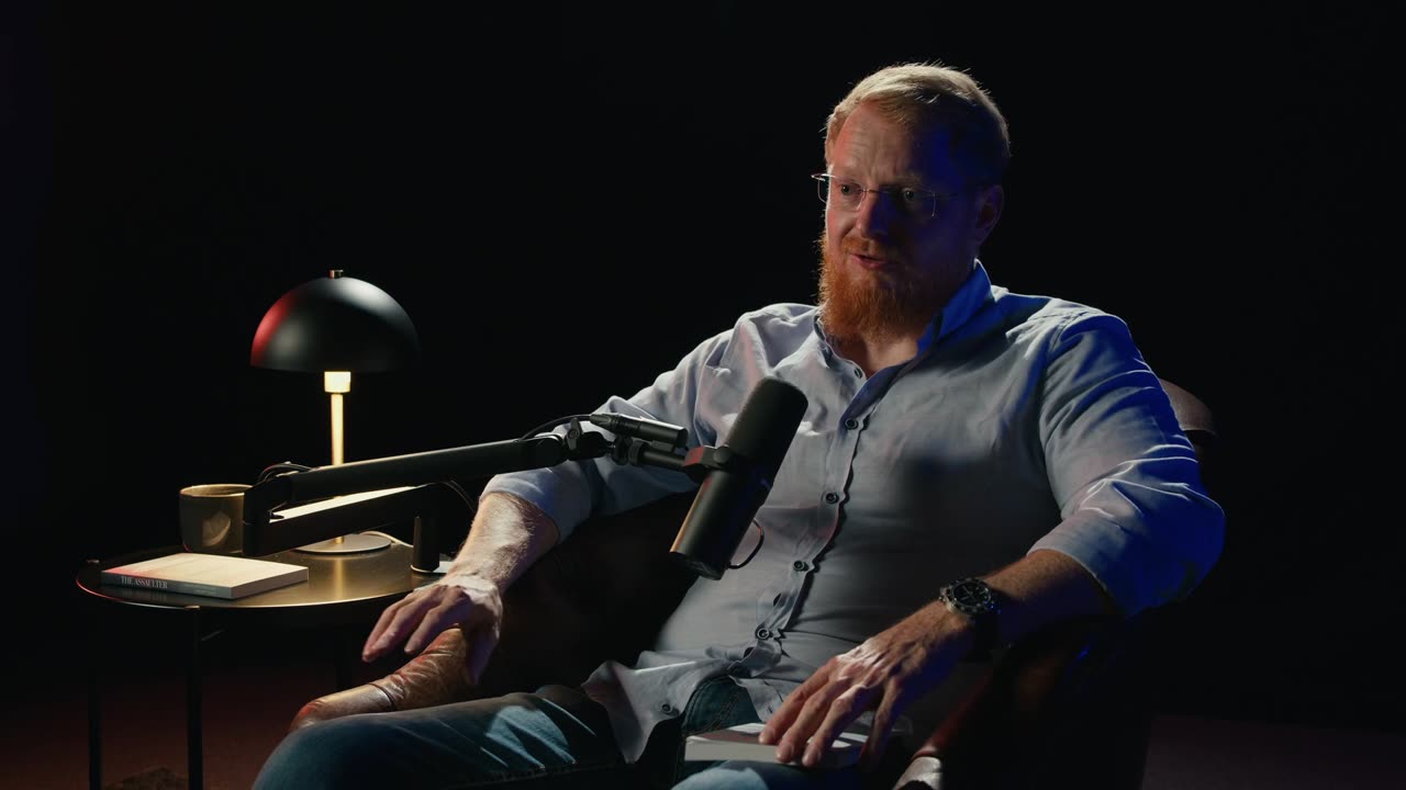 Standbild aus dem Dankesvideo: Christopher Wagner im Sessel am Mikrofon, neben ihm das Buch